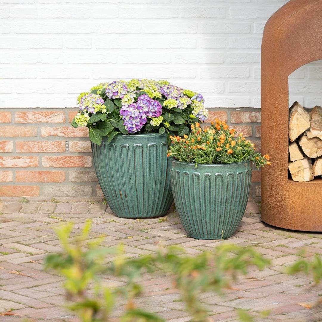 Two green planters with flowers against a brick wall.